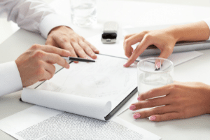 Image description: a promotional image for our consultancy inclusion services. It is two pairs of hands resting on a white table, pointing at different parts of documents between them, indicating active discussion. End of image description.